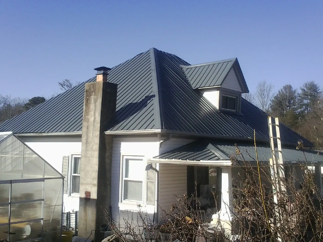Dark blue standing seam metal roof on a white farmhouse with dormer — Slate & Tile Roof Repair by Roofing Brothers in Pleasant Mount