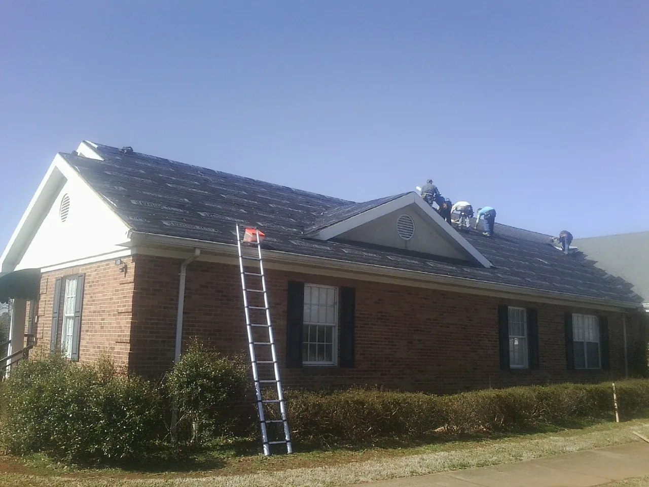Crew tearing shingles off a brick ranch roof with a ladder set — Emergency Roof Repair work by our crew in Pleasant Mount