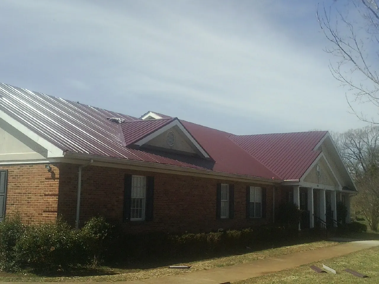Red metal roof with gabled entries on a long brick building, from a Hail Damage Roof Repair job in Pleasant Mount
