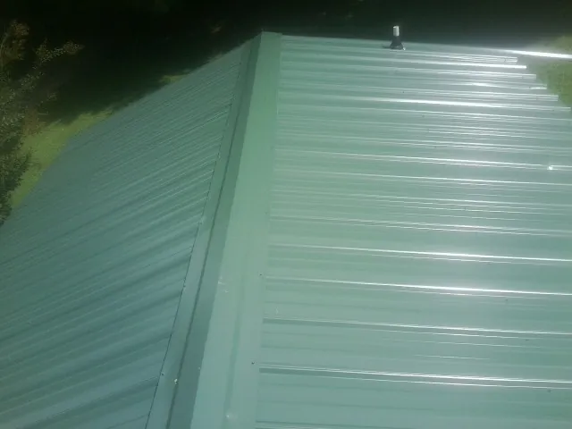 New green metal panels meeting at the ridge of a roof — Flat Roof Repair work by our crew in Pleasant Mount