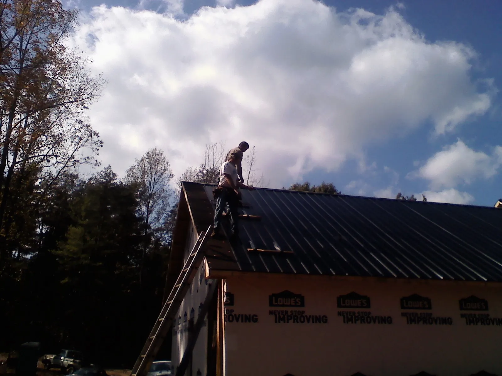 Roofer fastening dark metal panels high against a cloudy sky, from a Roof Inspection job in Pleasant Mount