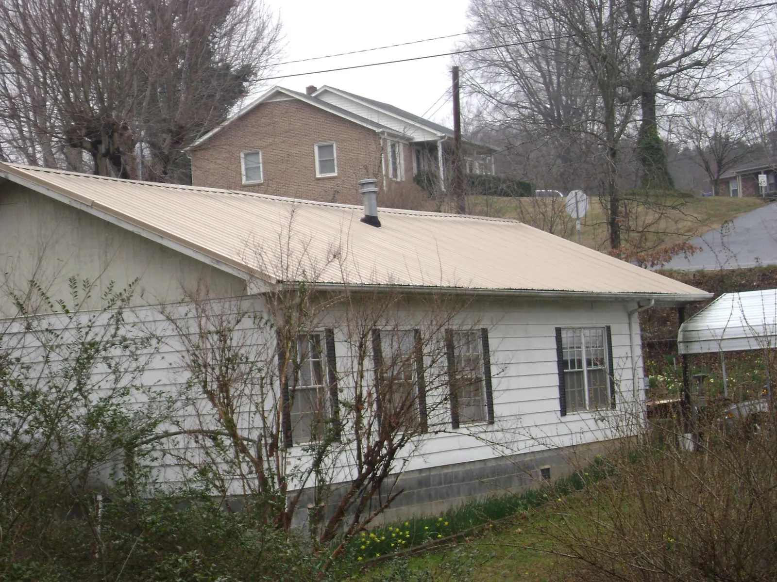 Tan metal roof on a white sided house set into a hillside — Commercial Roofing by Roofing Brothers in Pleasant Mount